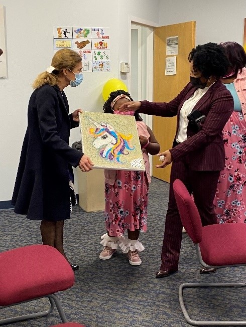 SW Tomi Handy hands Alivia a stained glass picture of a unicorn with Susan Bysiewicz 