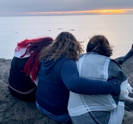 Youth hugging with a large body of water in the background.  They face away from the camera and look out on the water.