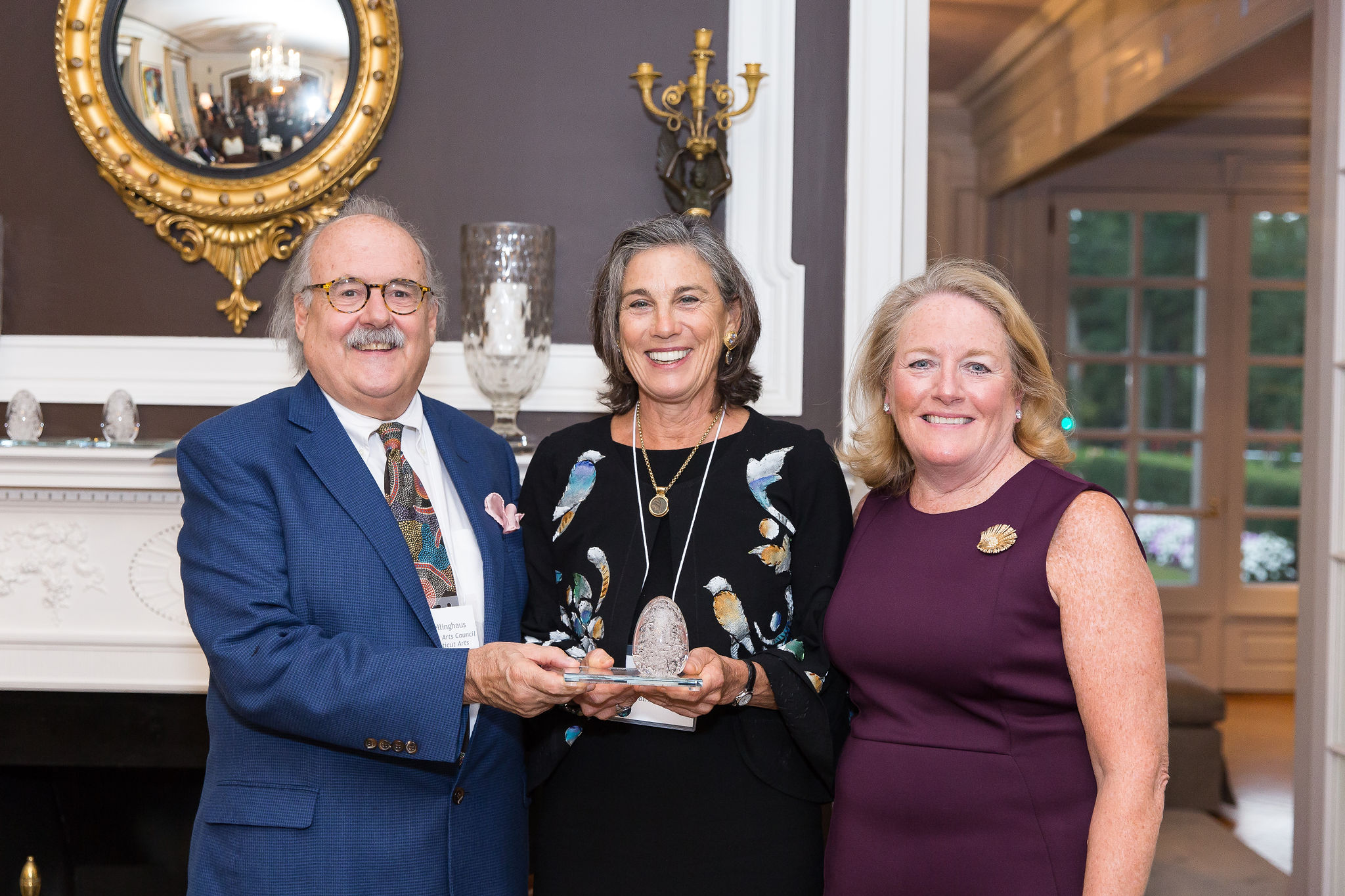 Awardee in the middle holding a glass sculpture award with supporting individuals on each side of her. 