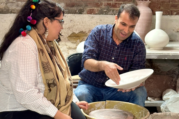 A student working with a master artist at a potting wheel. 