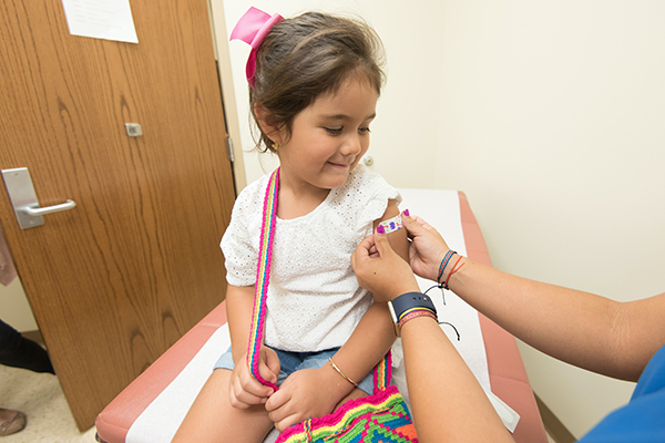 Young girl receiving Band-Aid from medical professional after COVID-19 Vaccine.