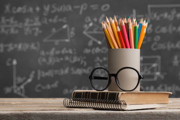 Pencil holder and eyeglasses sitting on book with blackboard in the background