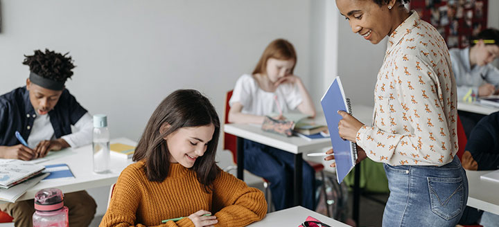 teacher looks over the shoulder of a young female student as she writes